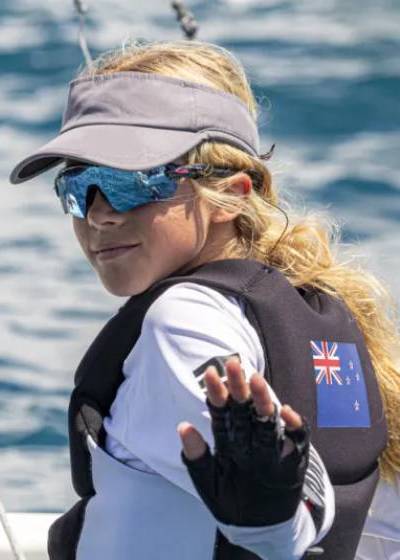 Person on a boat wearing a life jacket with a flag, sunglasses, and a visor.
