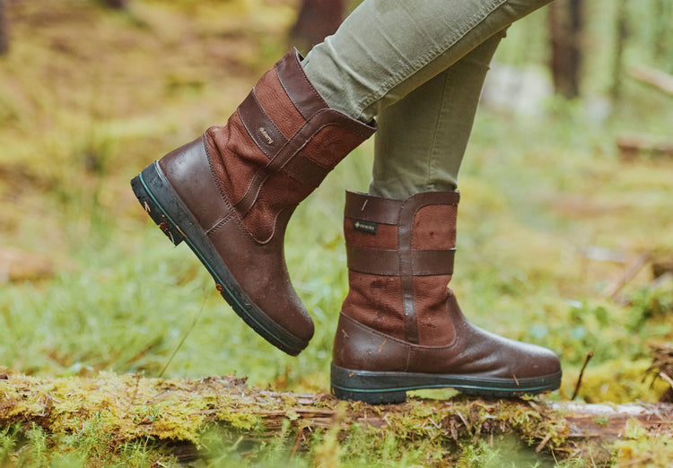 An on model image of a pair of Dubarry Ladies  Roscommon Country Boots, walnut brown short leather boots in a grassland